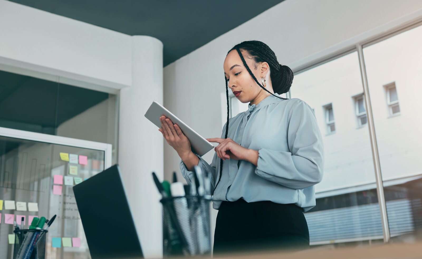 Professionnelle consultant une tablette dans un bureau, devant un tableau couvert de notes autocollantes