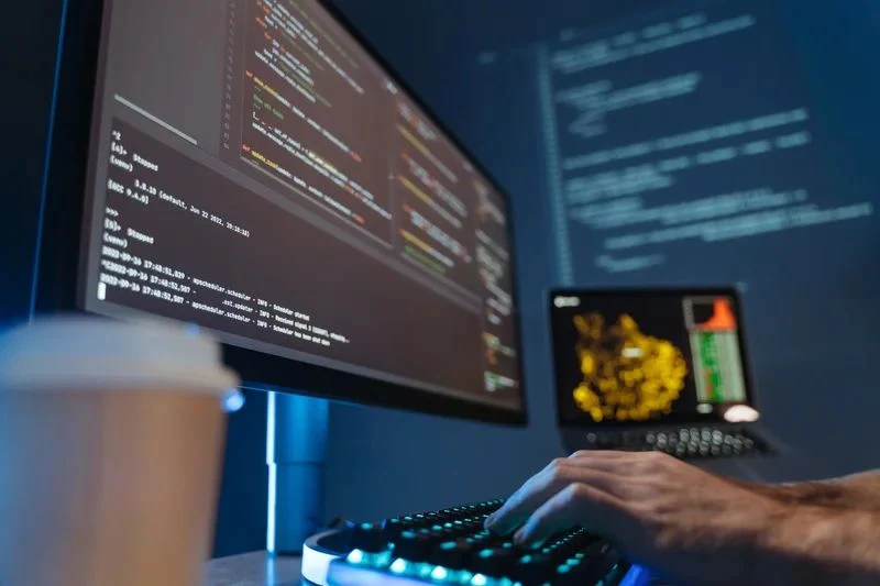 Développeur au clavier devant un écran de code et des journaux d’exécution.