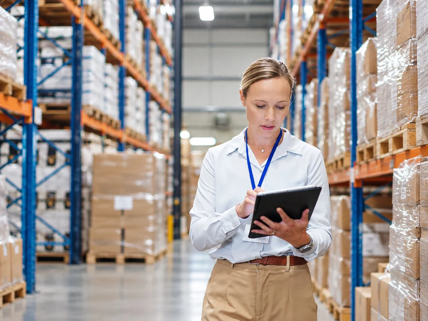 Responsable d’entrepôt consultant une tablette dans une allée de stockage, entre des palettes prêtes à l’expédition